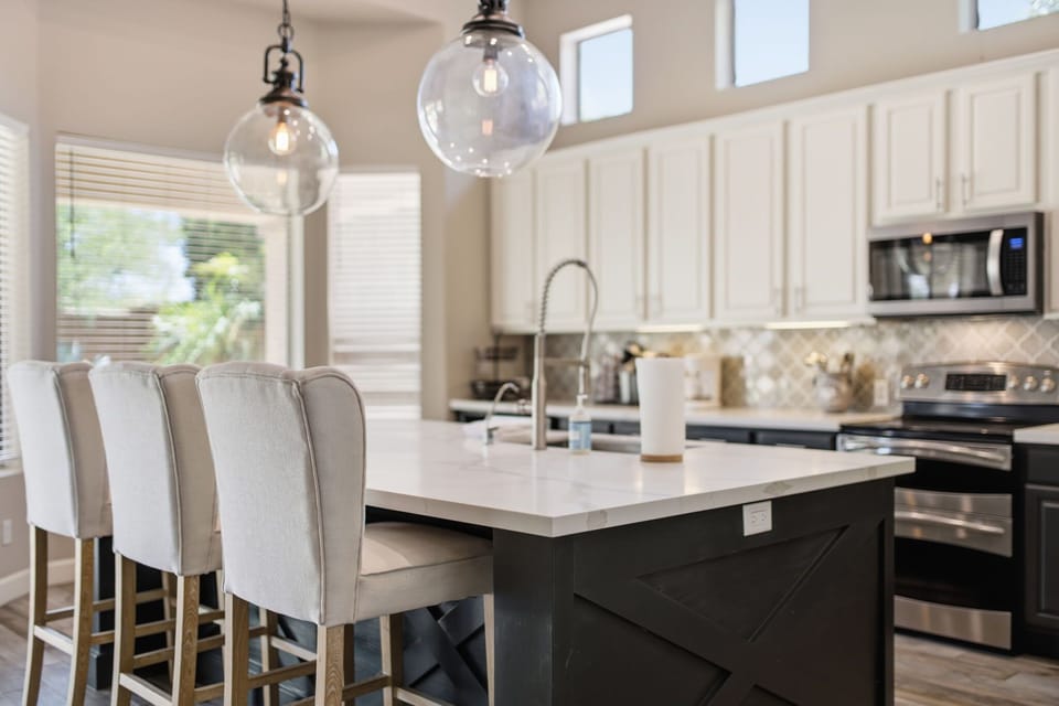 The kitchen's two-toned cabinetry and quartz counters wrap around a spacious island with seating for four, all finished with stainless steel appliances and a designer arabesque tile backsplash.