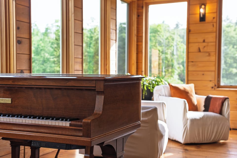 Sunlit great room with warm wood accents, piano, and sweeping meadow views.