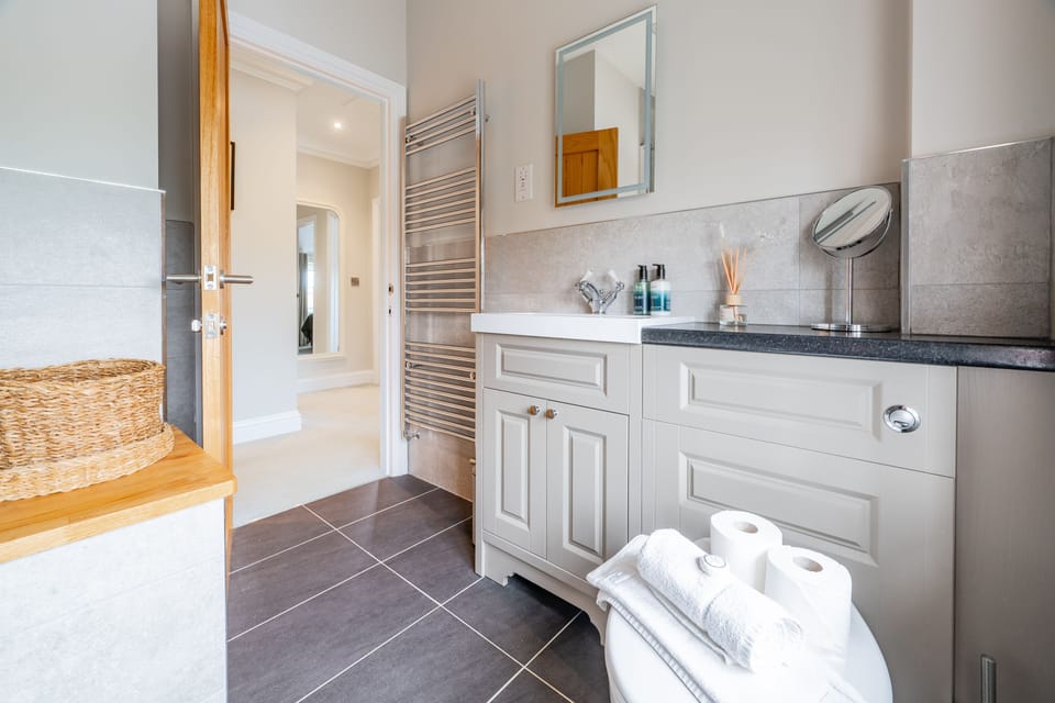 First floor: Family bathroom with a bath with handheld shower attachment and shower overhead, wash basin, heated towel rail and WC