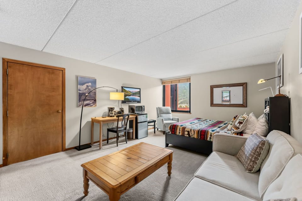 Your cozy studio combines comfort and convenience with a plush sofa, inviting bed with colorful throw, and a small kitchenette setup—perfect for relaxing after a day of mountain adventures.