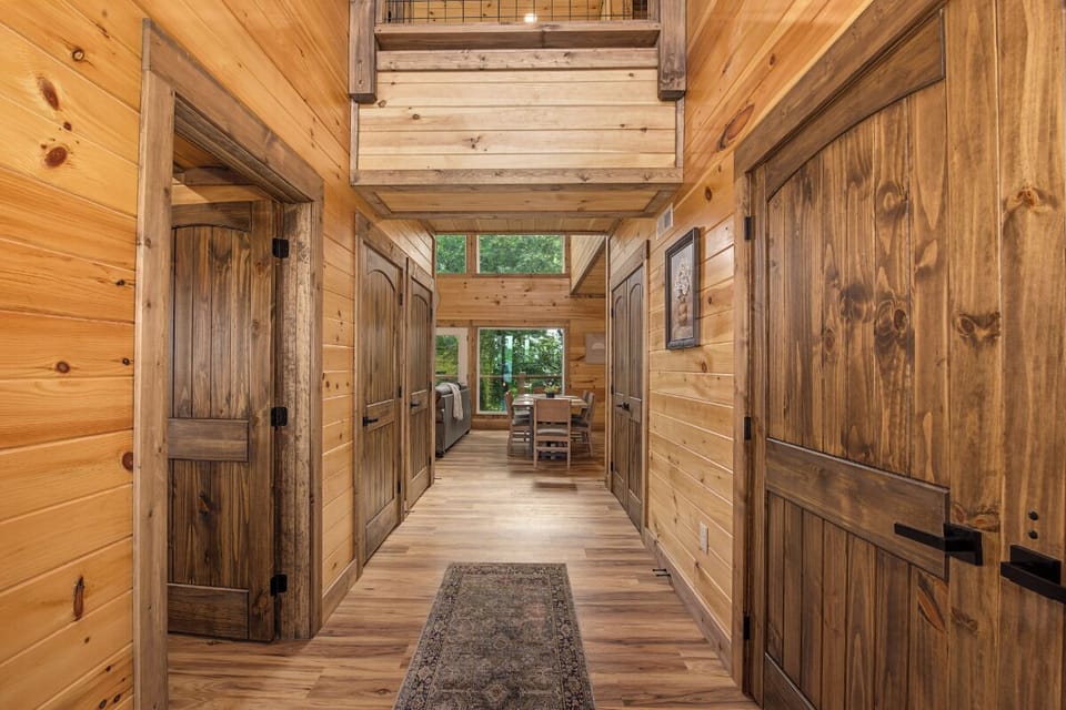 Step into warmth and craftsmanship—this inviting wood-lined hallway welcomes you with soaring ceilings, rustic doors, and glimpses of greenery ahead, setting the tone for your peaceful mountain escape.