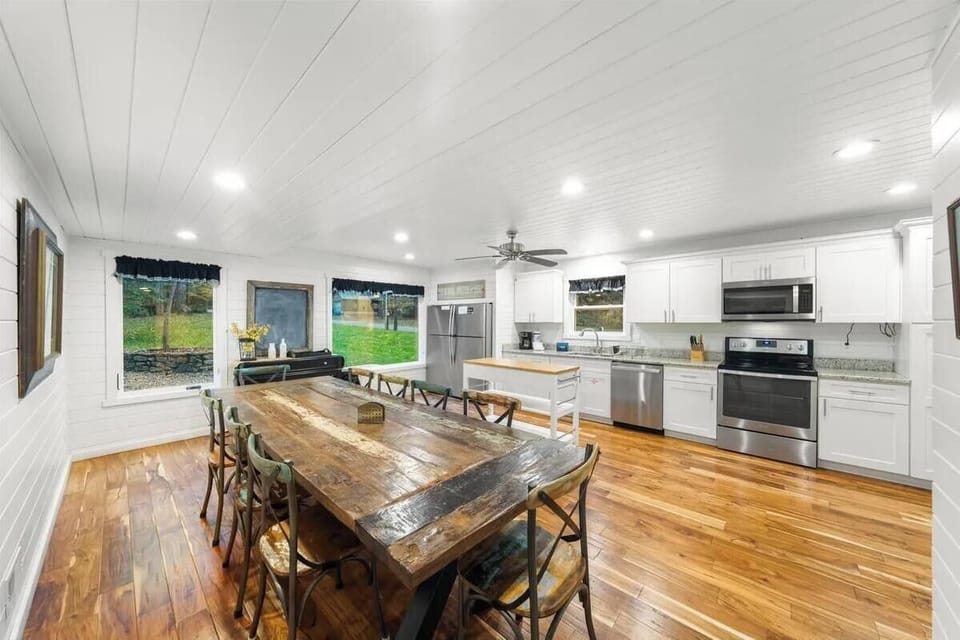 Gather around the rustic farmhouse table in your bright, open kitchen where wide windows frame peaceful garden views, making every meal feel like a country escape.