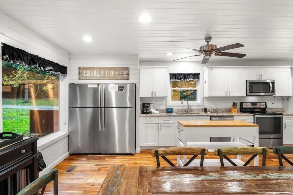 Bright farmhouse kitchen with stainless steel appliances and warm wood floors. Open layout perfect for cooking and gathering with loved ones around the rustic table.
