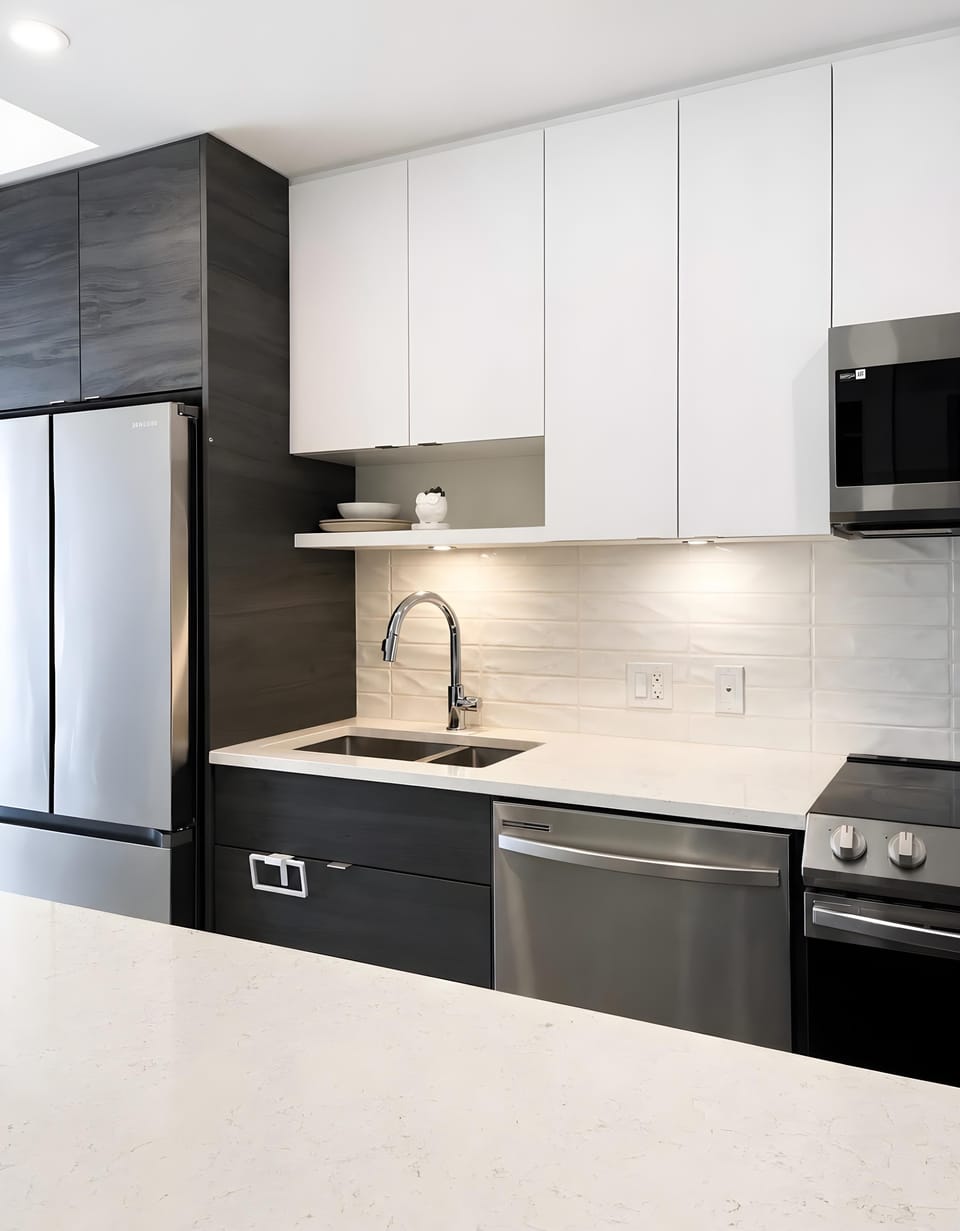 Sleek modern kitchen featuring dark lower cabinets, white upper storage, integrated lighting, and stainless steel appliances.