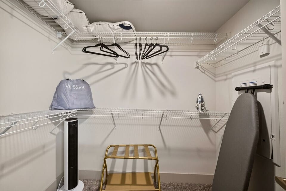 Spacious walk-in closet fully equipped with hangers, a luggage rack, iron, and ironing board for all your storage and travel needs.