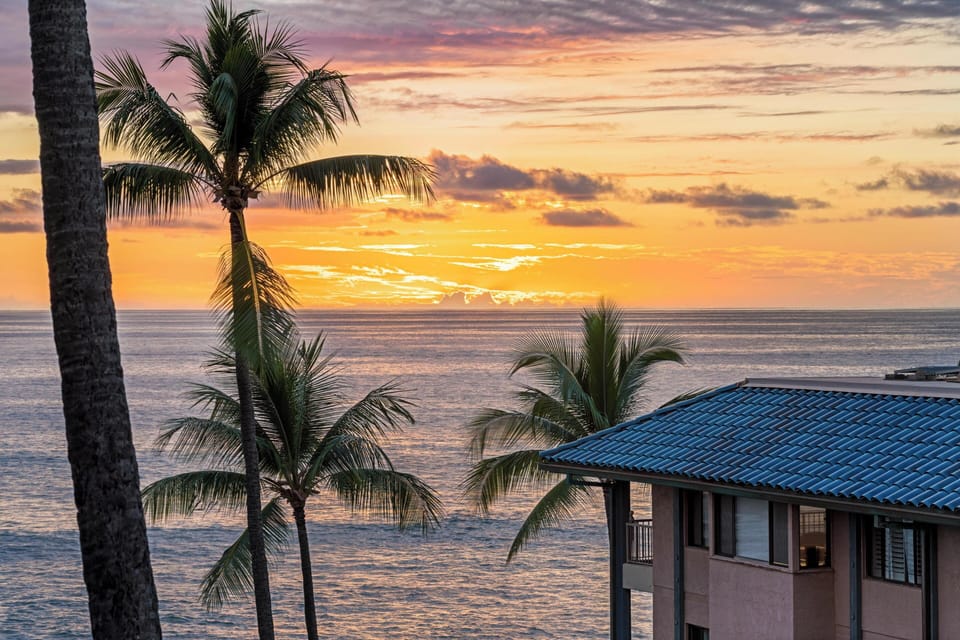 A stunning beachfront property with iconic palm trees and brilliant sunset colors painting the sky over the calm ocean waters.