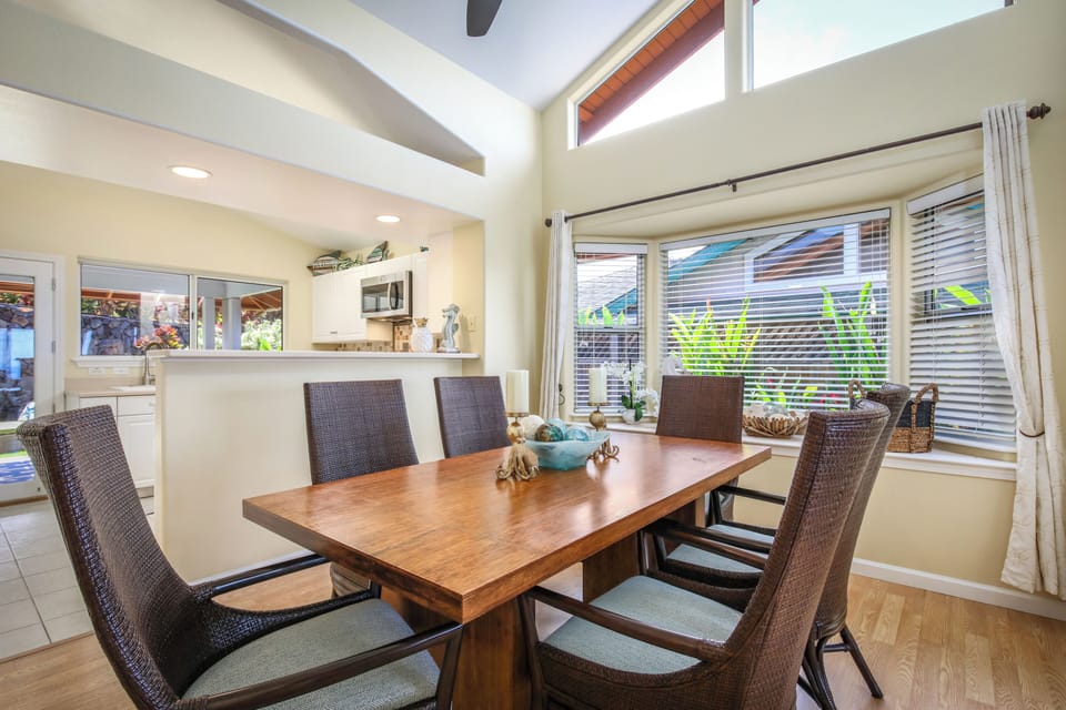 Gather around this elegant dining table with room for everyone. High ceilings and sunlight streaming through generous windows create a warm, open atmosphere perfect for your morning coffee or shared meals together.