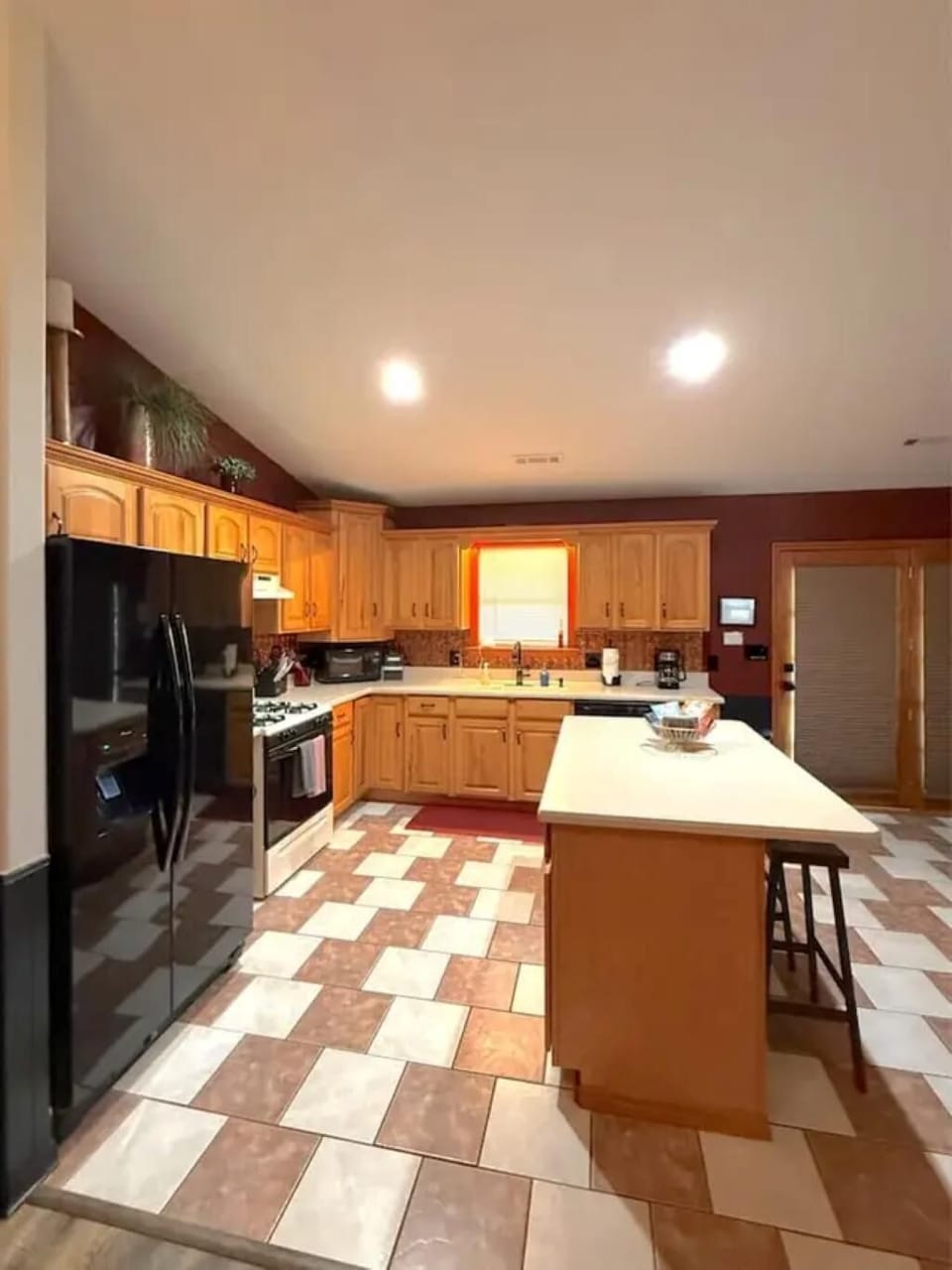 Spacious kitchen with honey oak cabinets, black appliances, white countertops, and two-tone tile flooring.