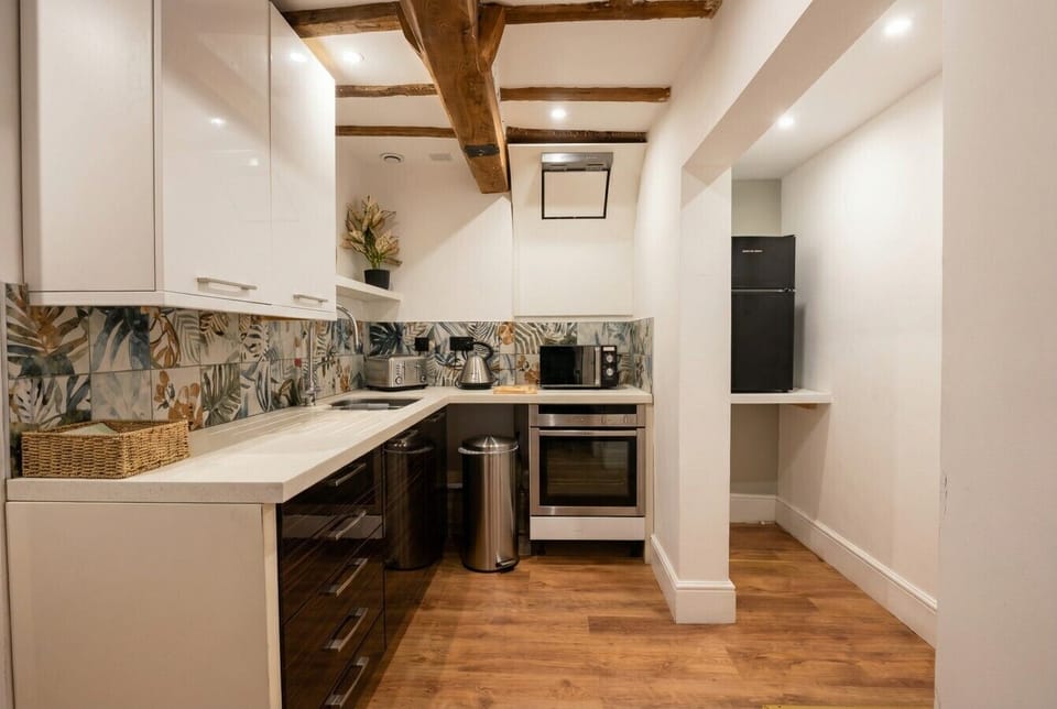 Botanical-tiled kitchen with a full oven and fridge tucked beneath original beams.