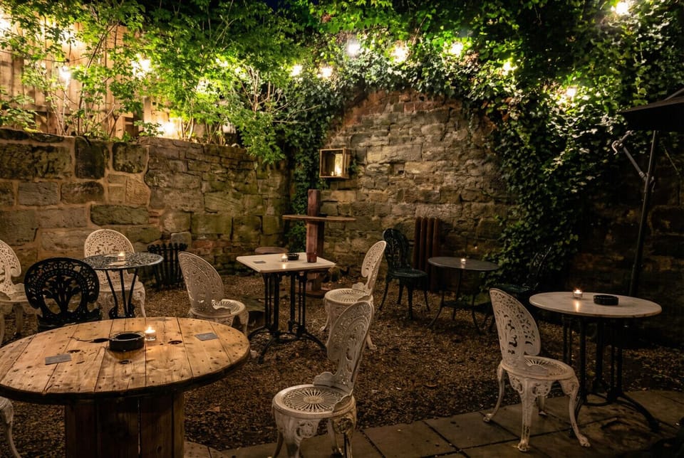 Candlelit iron bistro tables and festoon lights fill the ivy-draped courtyard garden for magical evenings outdoors.