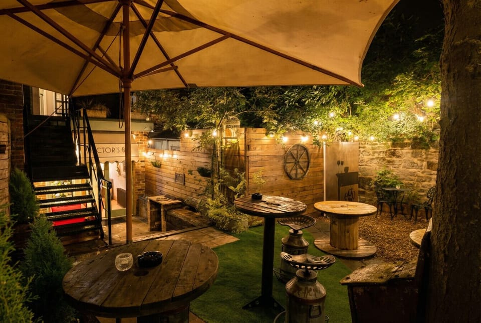 Hector`s Bar garden glows after dark, festoon lights strung above spool-table cocktails.