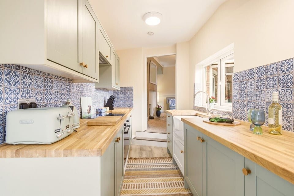 Galley kitchen with wooden worktops and blue patterned splashback.