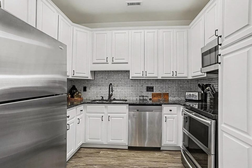 Bright white kitchen with granite counters, dishwasher, and stainless steel appliances