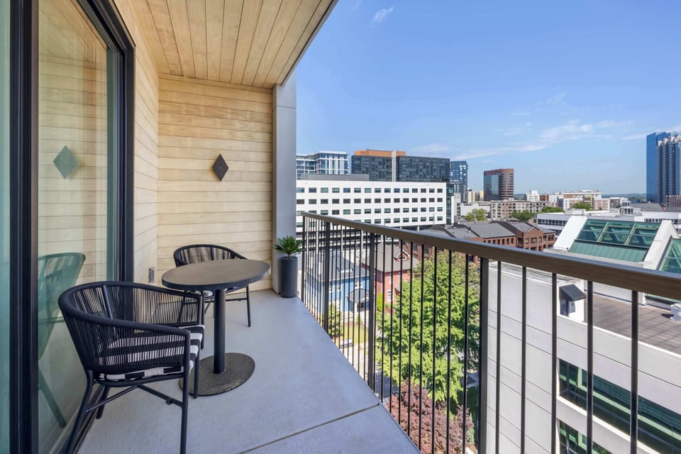 The private balcony offers a breezy urban escape with warm wood surrounds, seating for two and open skyline views of the city.