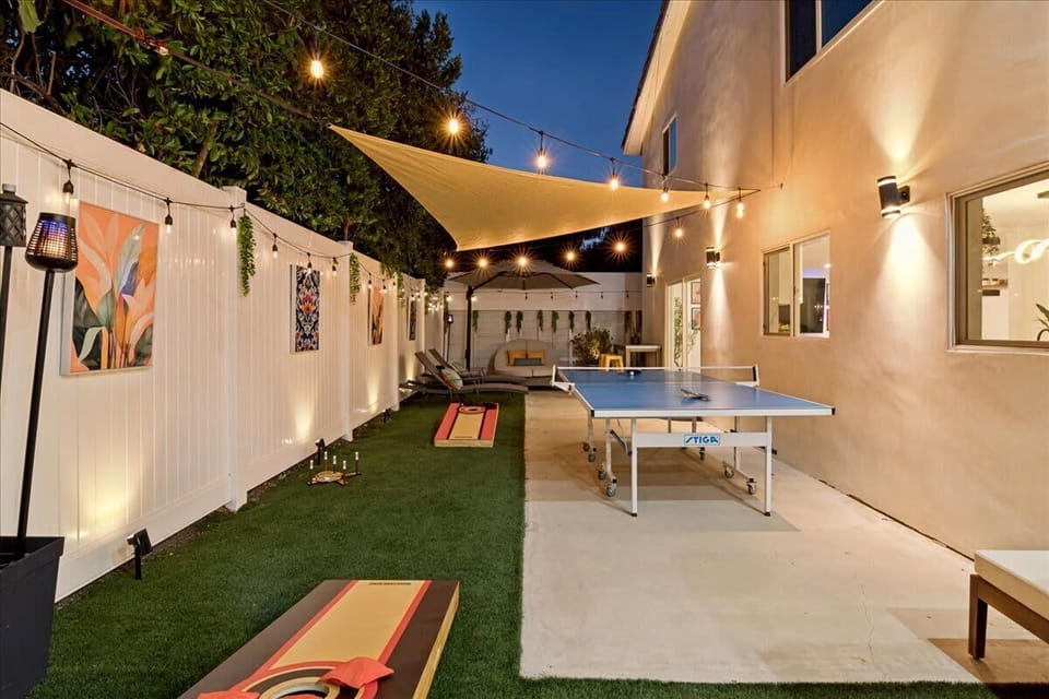 Awesome backyard outdoor space with games, accent lighting, a 65-inch television, and plenty of comfortable seating for people to enjoy