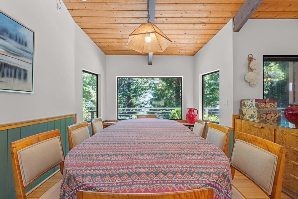 Seat your group of eight at the long dining table under vaulted beams, with the forest framed in three wide windows.