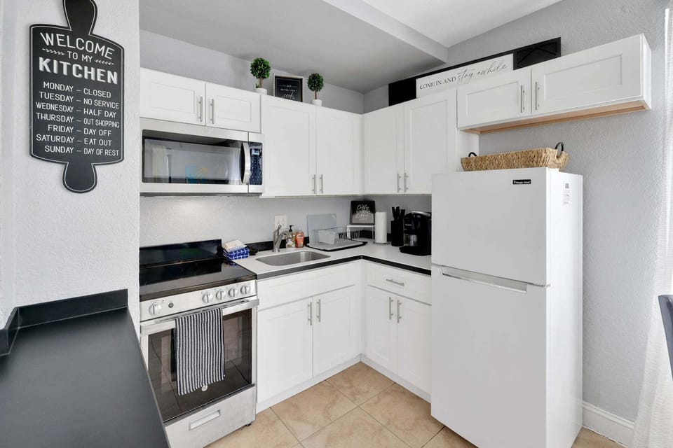 Cook with ease in a bright kitchen boasting white cabinetry, a full-sized refrigerator, a stove, an oven, and a microwave.
