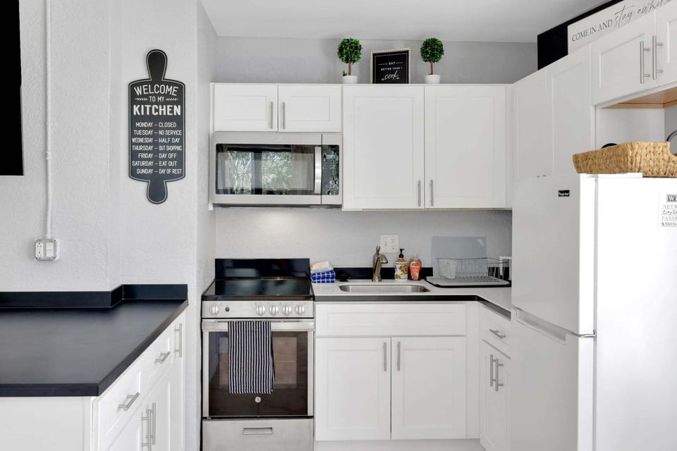 Cook with ease in a bright kitchen boasting white cabinetry, a full-sized refrigerator, a stove, an oven, and a microwave.