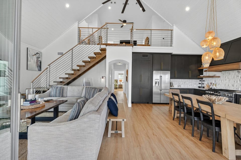 Open-concept living room with sectional sofa, dining area, kitchen, vaulted ceiling, and loft stairs