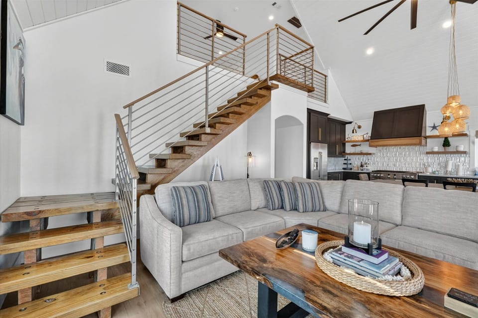 Living room with sectional sofa, loft staircase, wood coffee table, and open kitchen connection.