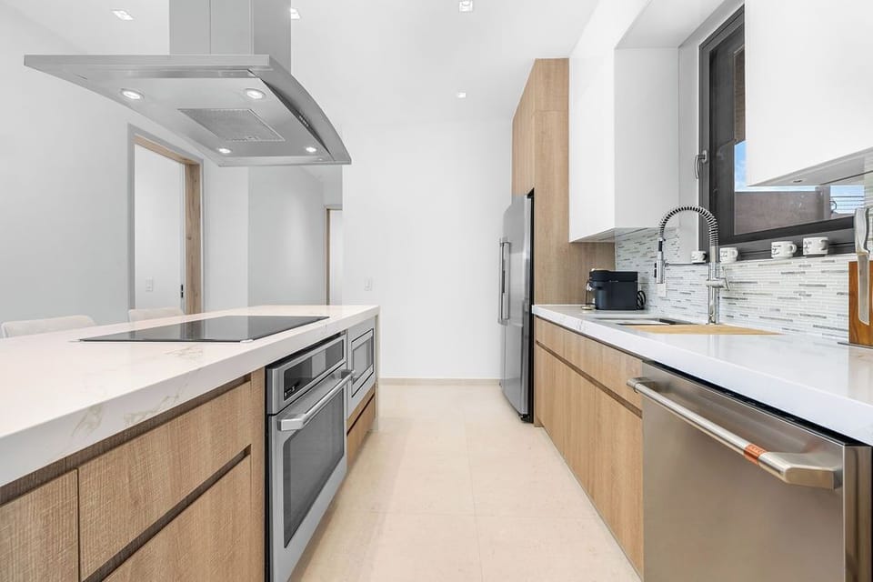 Prep breakfast on the marble-patterned island bathed in natural light, with sleek stainless appliances, striking white-and-wood cabinetry, and a subway tile backsplash that adds just the right touch of personality.
