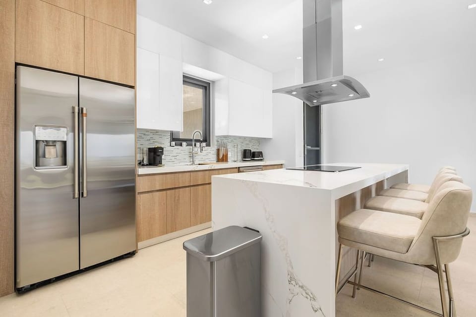 Prep breakfast on the marble-patterned island bathed in natural light, with sleek stainless appliances, striking white-and-wood cabinetry, and a subway tile backsplash that adds just the right touch of personality.