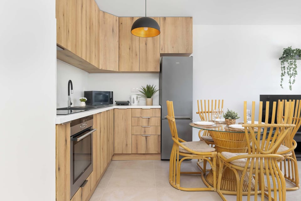 A modern kitchenette with wooden cabinets and a dining table. The space is bright and fully equipped.