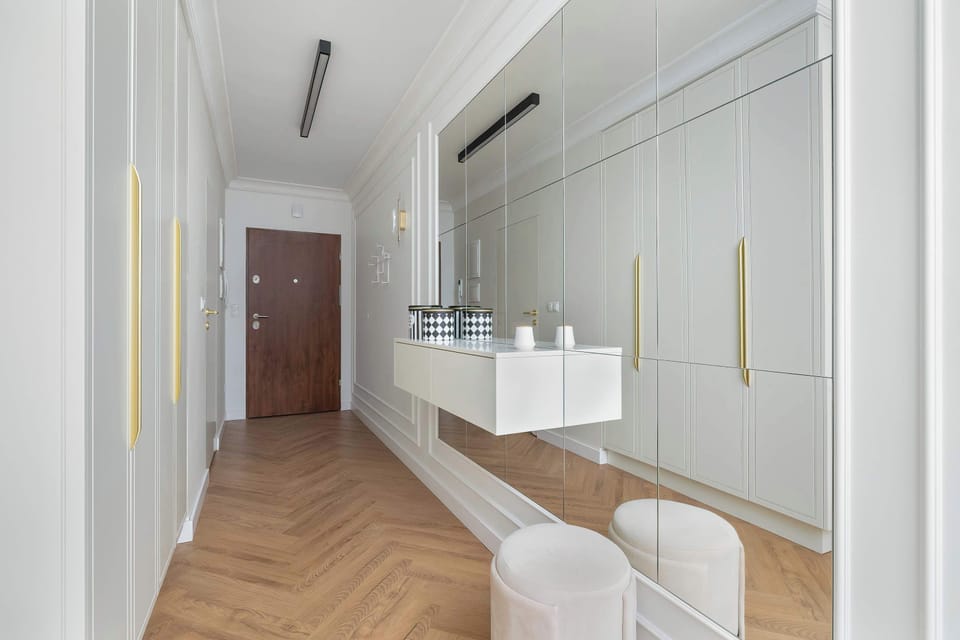 An entryway perspective showcasing a large mirrored sliding wardrobe and herringbone wooden floors. Soft lighting illuminates the path toward the main living areas.