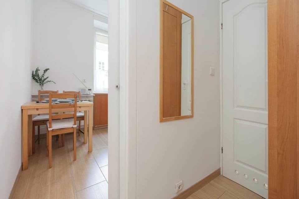 A doorway opens up to reveal a separate dining area equipped with a classic wooden table and chairs. A mirror mounted on the hallway wall adds depth to the transitional corridor.