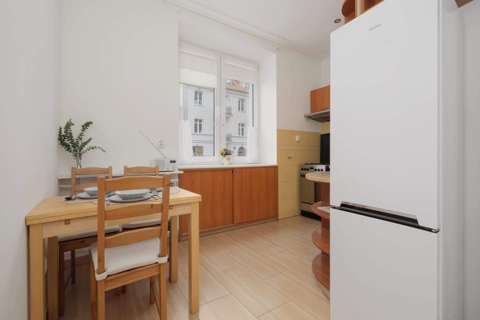 Looking from the opposite side of the kitchen reveals the placement of a freestanding white refrigerator next to the cabinetry. The light-colored floor tiles complement the warm wood tones of the furniture.