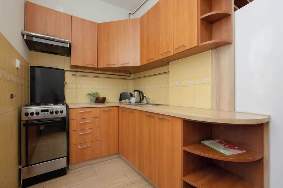 A compact, separate kitchen features warm wooden cabinetry arranged in an efficient L-shaped configuration. Standard appliances, including a classic gas stove and oven, are integrated into the setup.