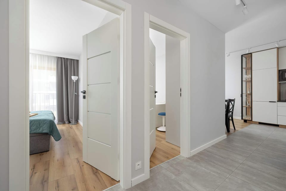 A viewpoint from the apartment's entrance hall shows open doorways leading into the bright living areas and bedrooms. Light wood flooring runs continuously through the spaces, enhancing the open feel.