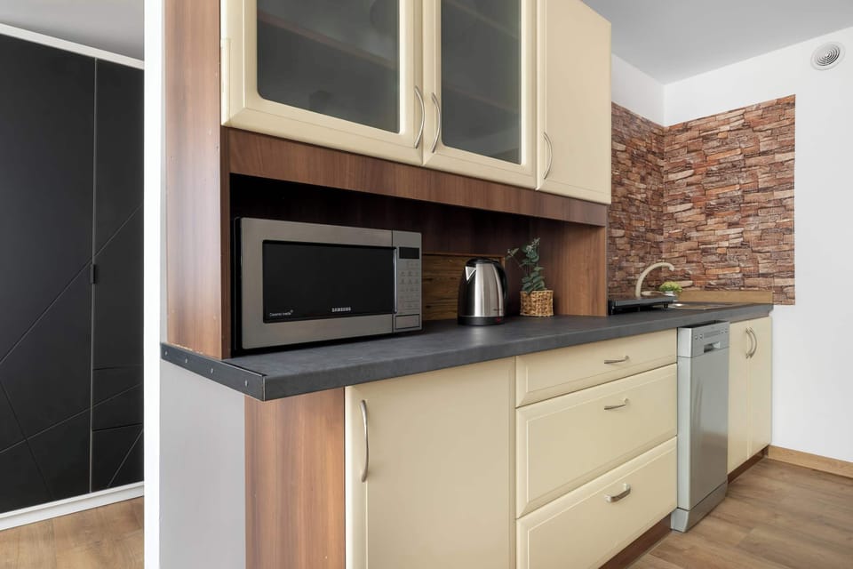 A compact kitchen setup includes upper glass-front cabinets, lower drawers, and an integrated microwave. Brick-style wallpaper adds character to the counter space.