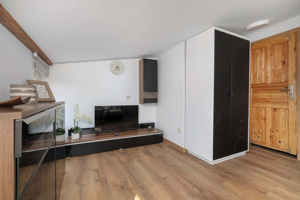 A living room perspective looks toward a TV media console and a solid wooden interior door. Simple contemporary furniture maintains an airy layout.
