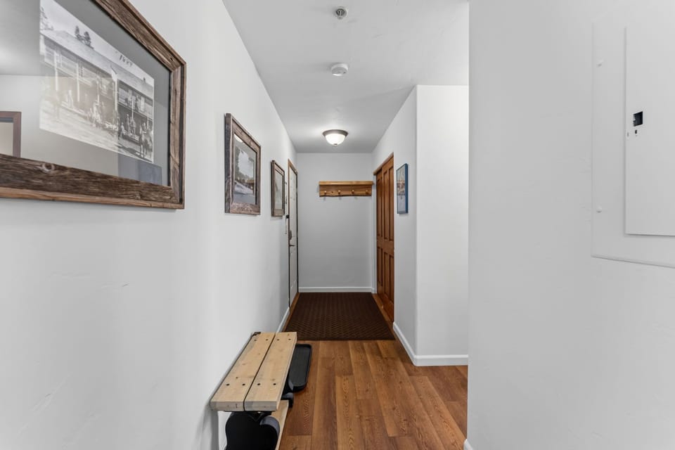 Step inside a welcoming hallway with warm wood floors, vintage-inspired framed photos lining the walls, and a handy bench for gear and boots—your home base for mountain adventures.