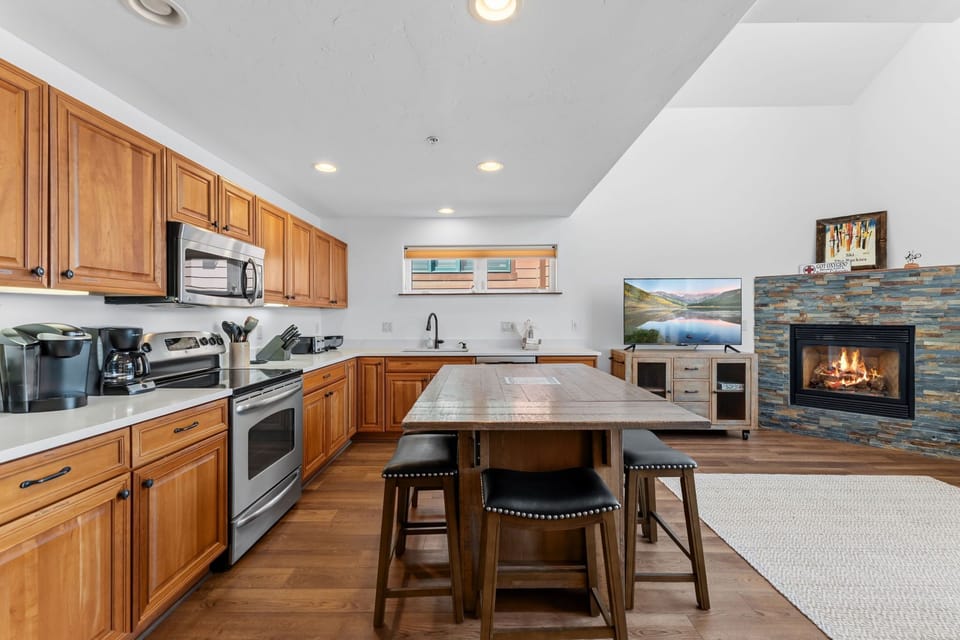 Your open kitchen features warm wood cabinetry, modern appliances, and a spacious island for cooking and gathering. Cozy up by the stone fireplace in the adjacent living area after a day of adventure.