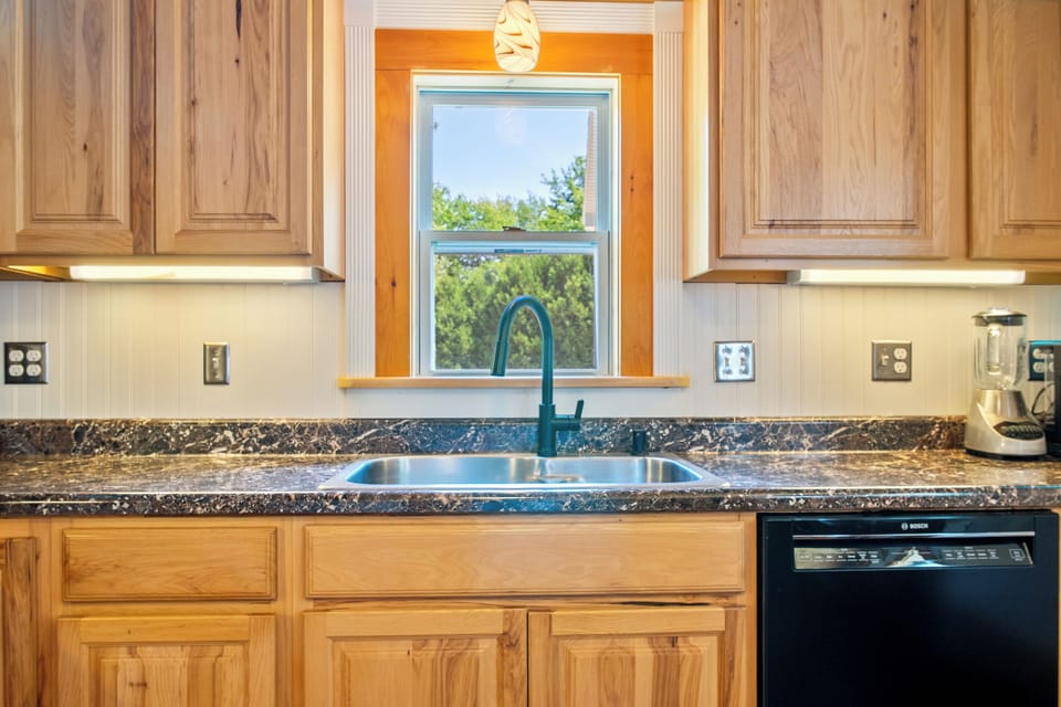 Clean up easily using the premium Bosch dishwasher integrated below the kitchen counter. This wider perspective reveals the abundant solid wood cabinetry storage, under-cabinet task lighting, and a countertop blender for your morning smoothies.