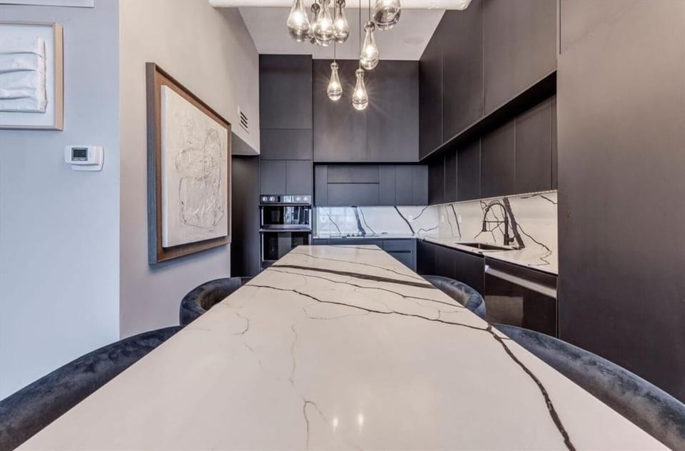 Close-up of the dining's dramatic marble island with velvet seating, framed by matte black cabinetry and a matching marble backsplash. Built-in appliances and sculptural pendant lighting complete this sleek, fully equipped culinary space.