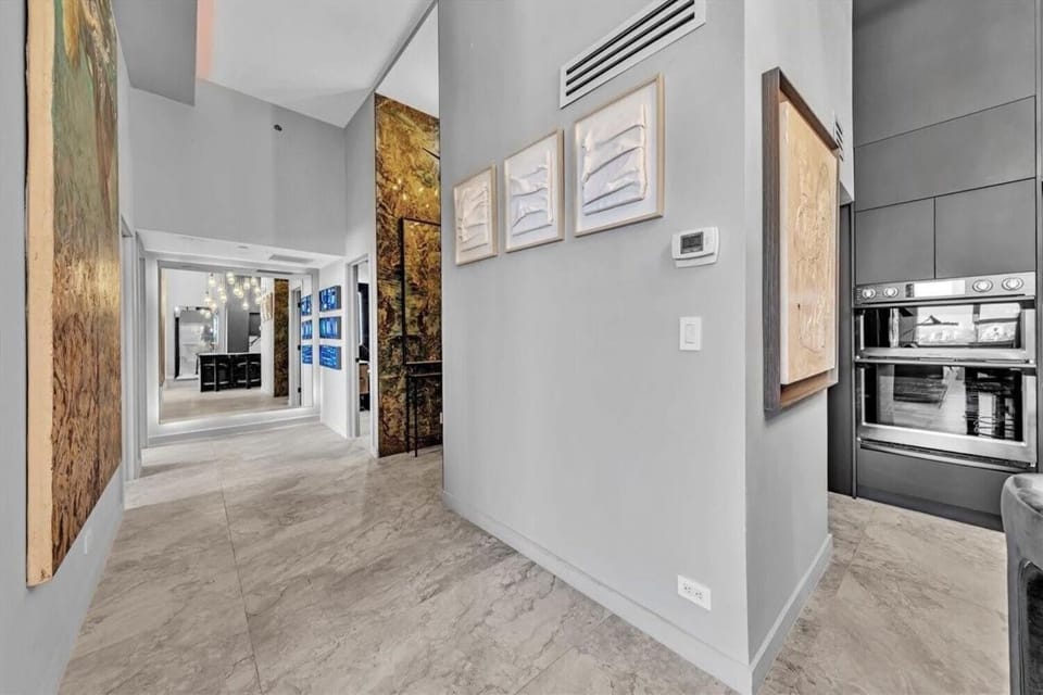Art-lined entry hallway with gallery-style framed pieces and dramatic floor-to-ceiling artwork throughout. Polished marble floors and soaring ceilings guide you through this curated space, connecting the kitchen and living areas in style.