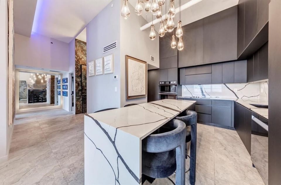Designer kitchen showcasing dramatic marble countertops and backsplash, matte black cabinetry, and plush velvet bar stools at the island. A cascading pendant light installation adds sparkle, making this space as beautiful as it is functional.