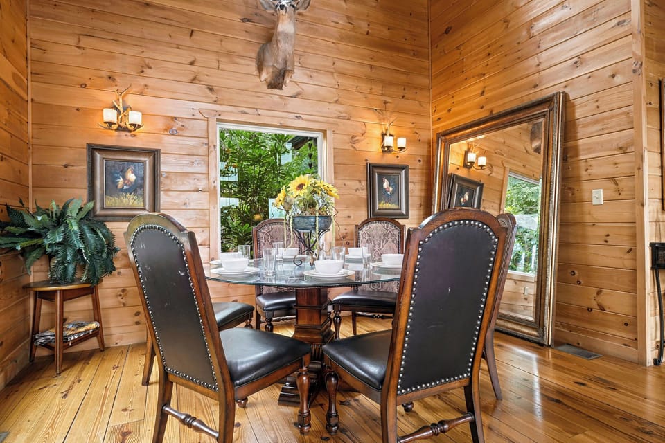 Gather around this elegant dining table beneath rustic wood beams and warm antler lighting. Through large windows, natural greenery frames your meals in a cozy, nature-inspired setting.