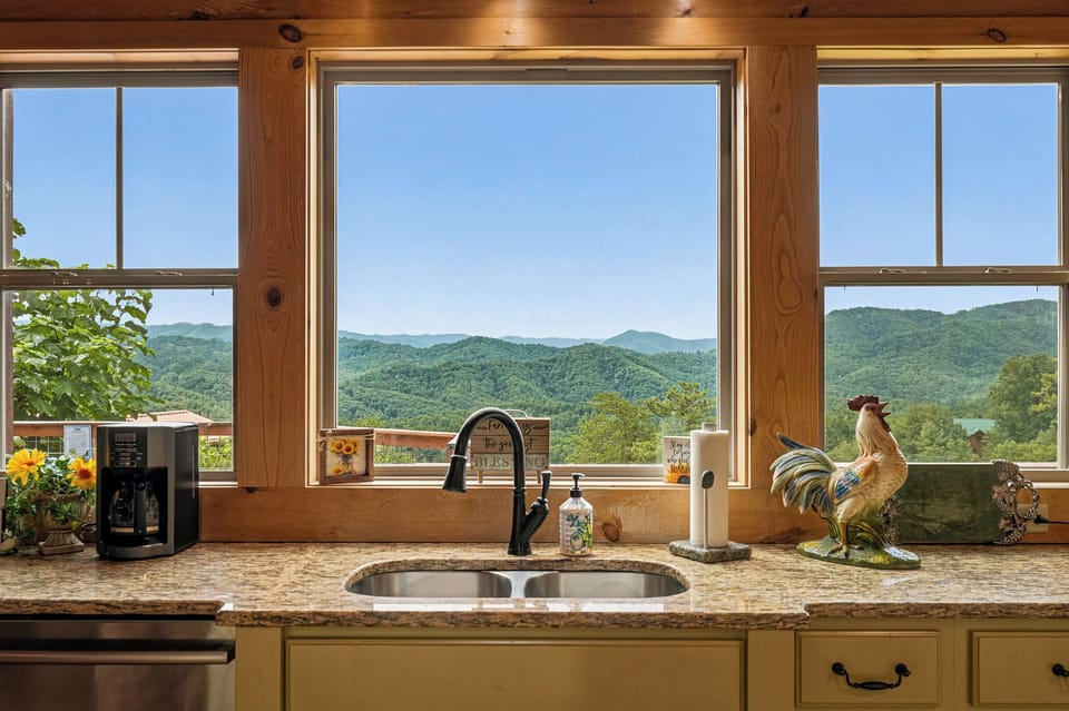 Savor your morning coffee at this kitchen sink with sweeping mountain vistas framed by rustic wood accents and sunlit skies.