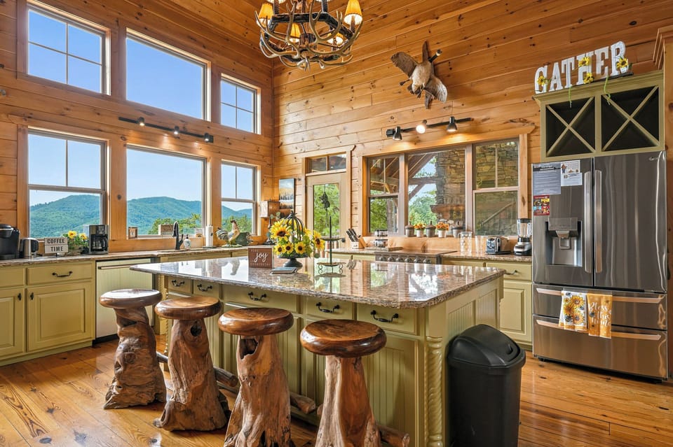 Gather in this stunning rustic kitchen featuring sweeping mountain views, a spacious island with unique log stools, and all the warmth of natural wood surrounding you.