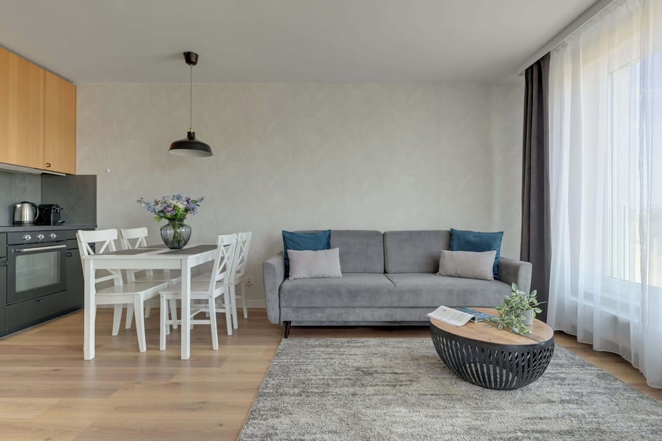 Apartament oferuje jasny salon z rozkładaną sofą, telewizorem, klimatyzacją oraz częścią jadalnianą. Duże przeszklenia prowadzą na przestronny balkon z meblami wypoczynkowymi i widokiem na okolicę.
