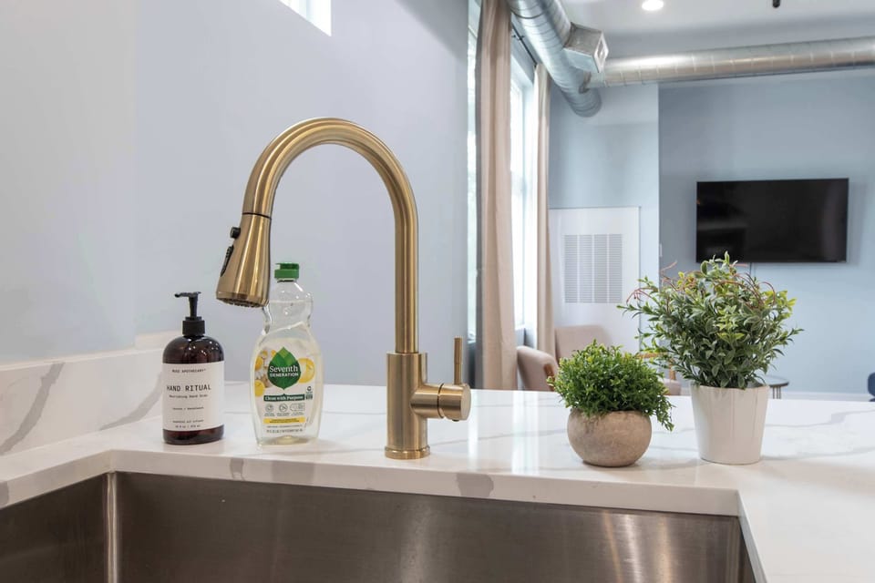 Kitchen sink w/ gold faucet overlooking a bright window.
