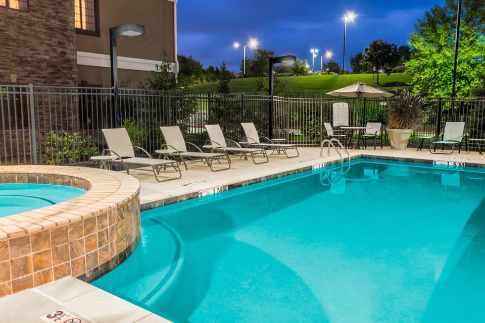 Outdoor pool lit at night with lounge chairs and the hot tub visible to the right