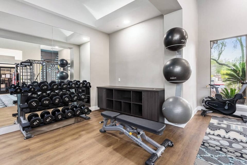 Bright on-site fitness room with weights, bench, mirrors, and natural light