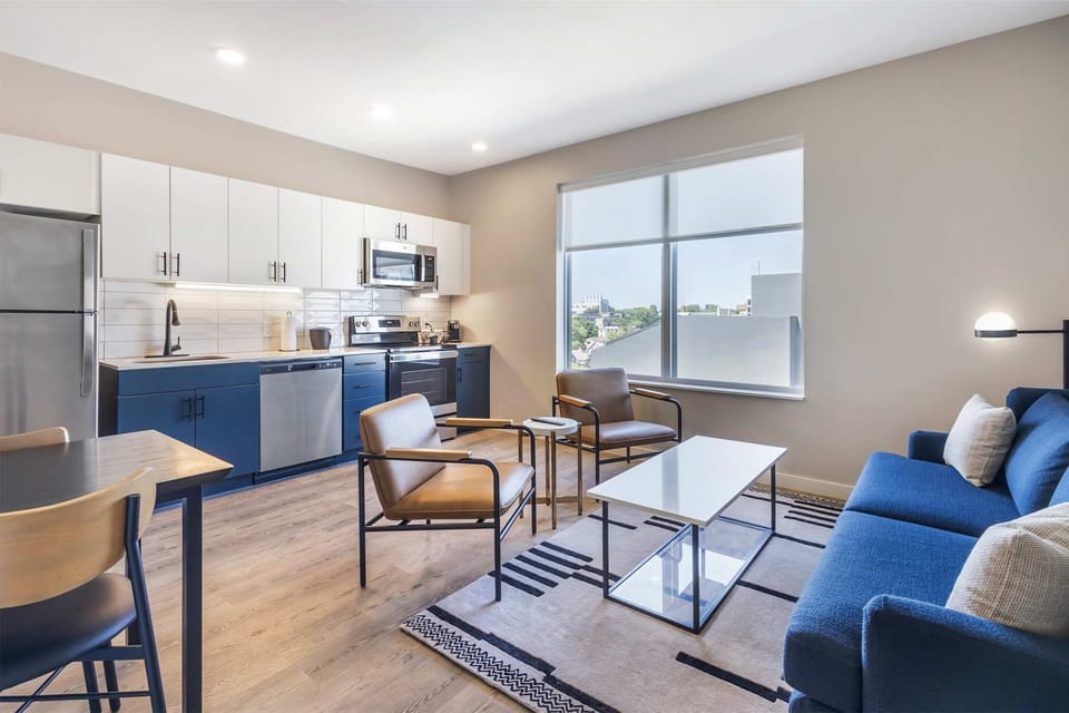 Bright, modern open-concept living with stylish seating, a fully equipped kitchen, and oversized windows framing the city view.