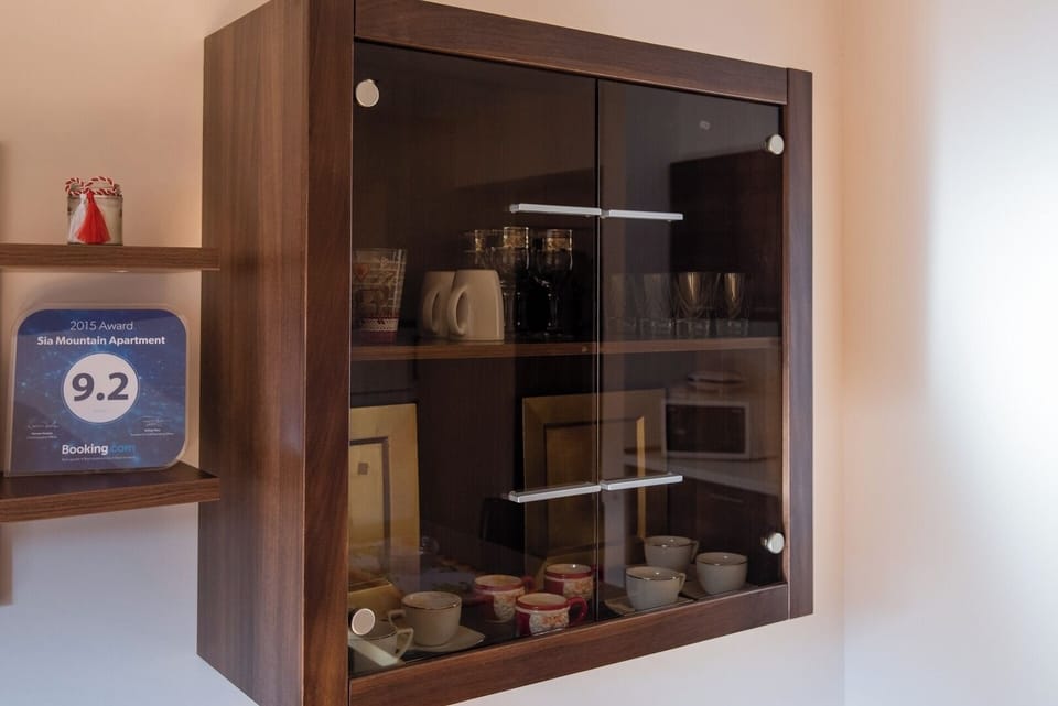 Glass-fronted display cabinet stocked with ceramic tableware, cups, glasses and a coffee maker. Thoughtfully equipped kitchen with everything needed for a comfortable stay in Sia Apartment, Predeal.