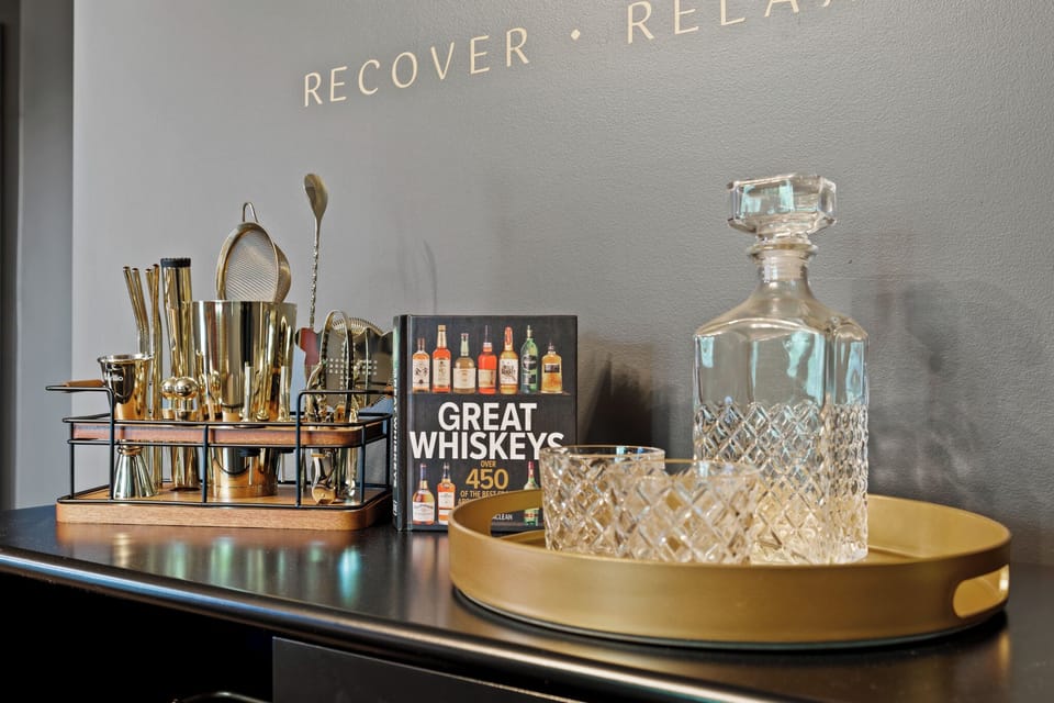 The speakeasy area has a brass chandelier, leather barstools + whiskey bar cart